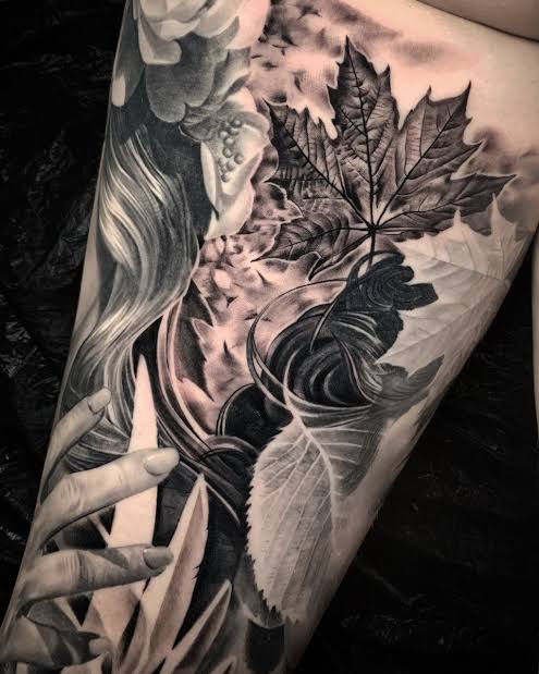 Black and gray maple leaves, flowing ribbons, and a graceful hand cover the thigh.