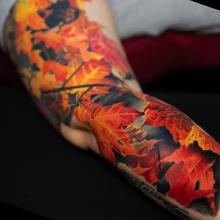 Fiery red and orange maple leaves flow through smoky black shading from shoulder to wrist.