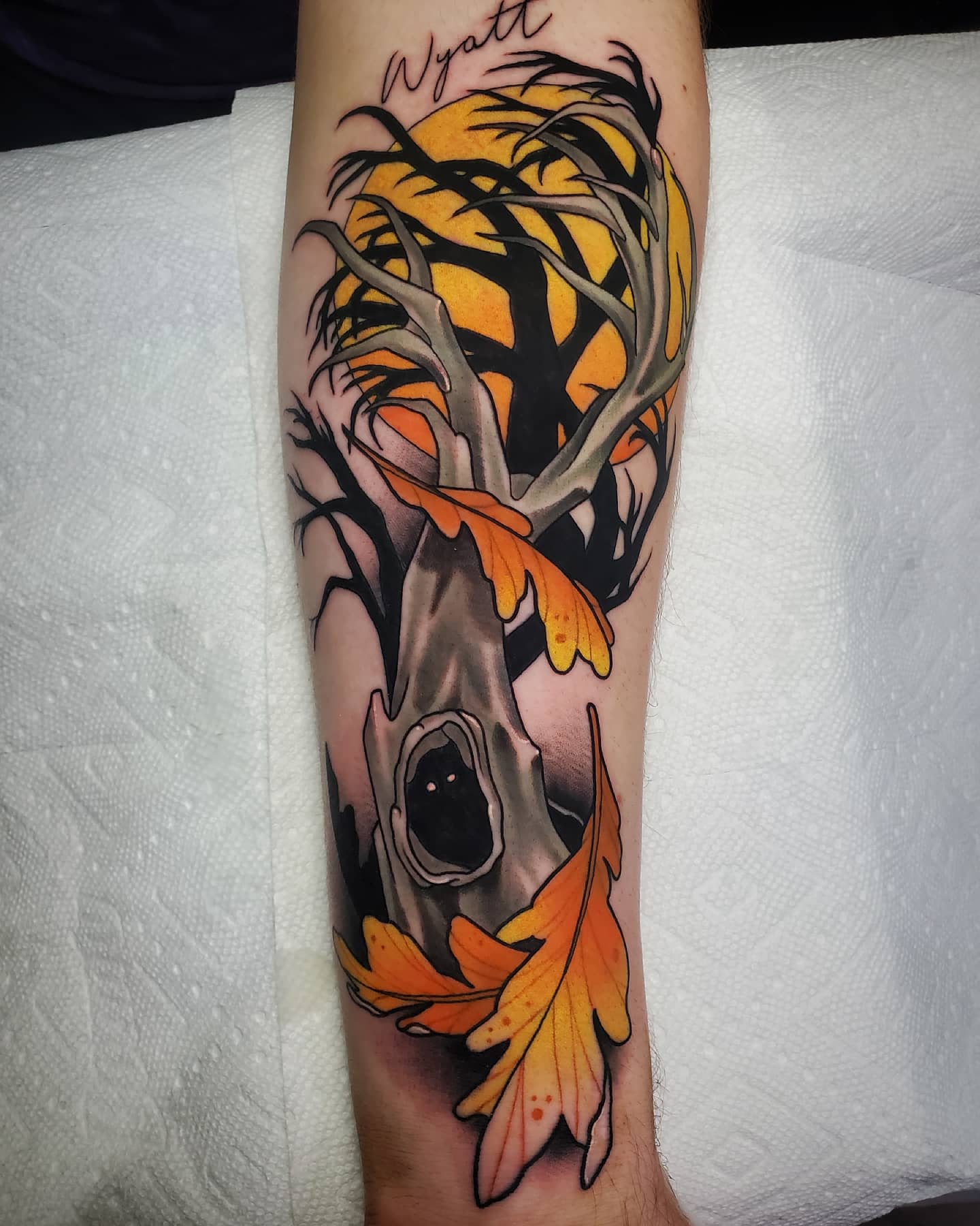 A hollow tree, glowing moon, and fallen orange leaves create a haunted forearm scene.