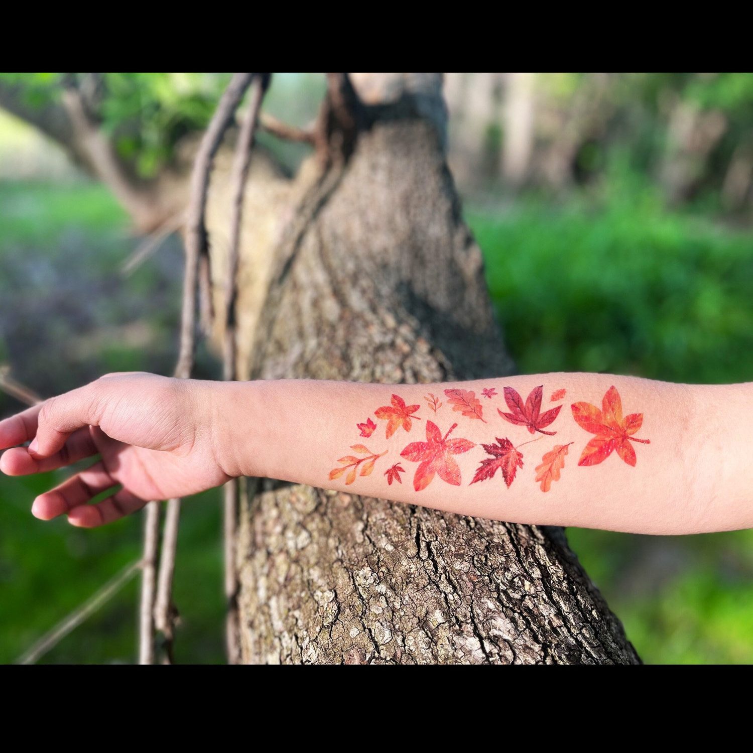 Red and orange autumn leaves spread across the forearm in a playful medium sized tattoo.
