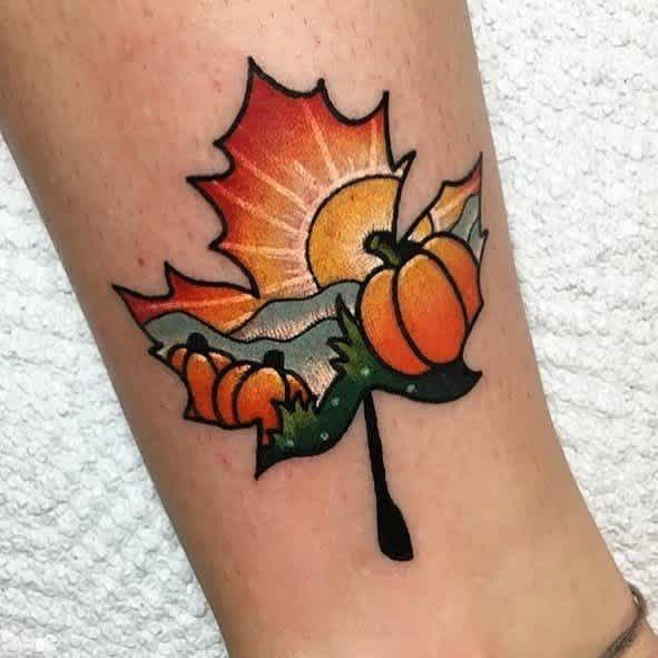 Orange pumpkins and fiery maple leaves create a compact autumn ankle tattoo.