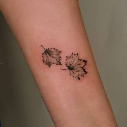 Two petite maple leaves with soft black shading sit side by side on the inner arm.