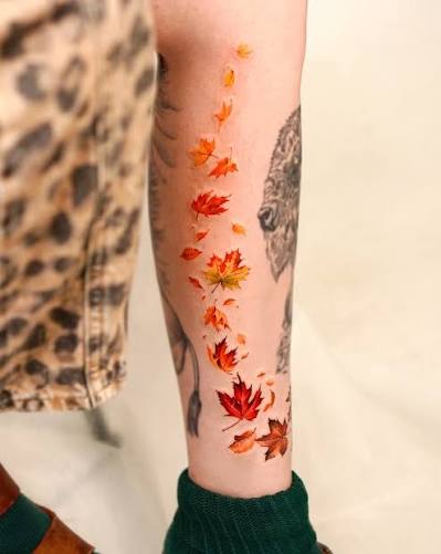 Tiny autumn leaves form a bright watercolor trail down the forearm in soft orange, red, and yellow.