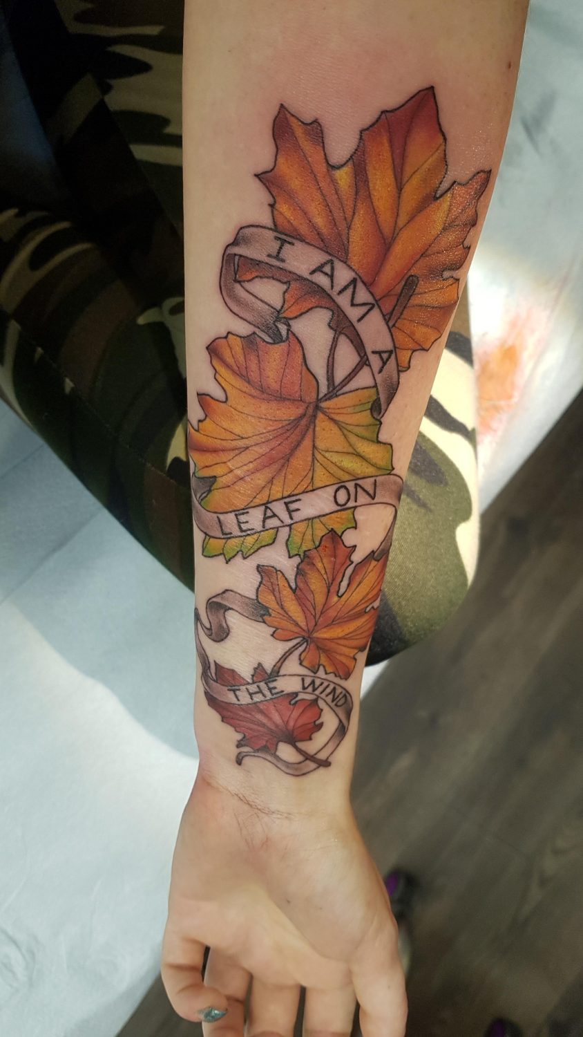 Glowing maple leaves surround a ribbon reading “I am a leaf on the wind” along the inner forearm.