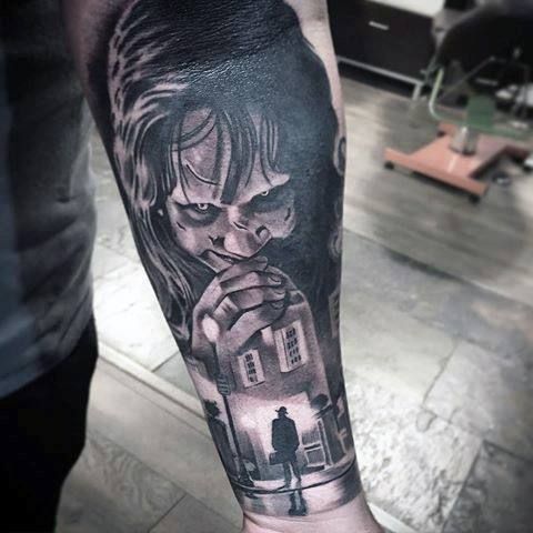 Black and gray forearm tattoo of Chucky with a scarred face and clasped hands.