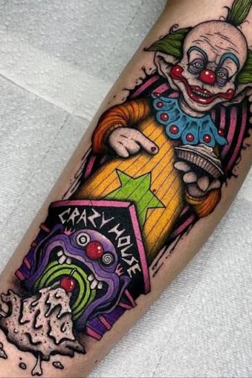 Colorful forearm tattoo of a grinning Killer Klowns clown with a small creature bursting out below.