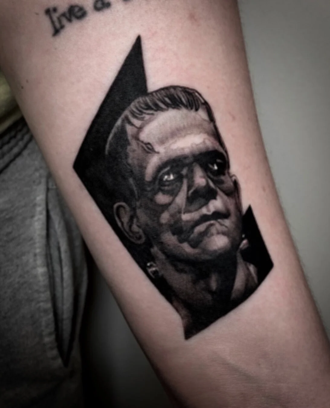 Large black and gray forearm portrait tattoo of a stern face against a dark backdrop.