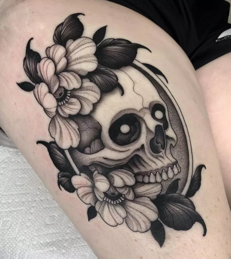 Skull nestled among soft flowers and dark leaves on the thigh with dotwork shading