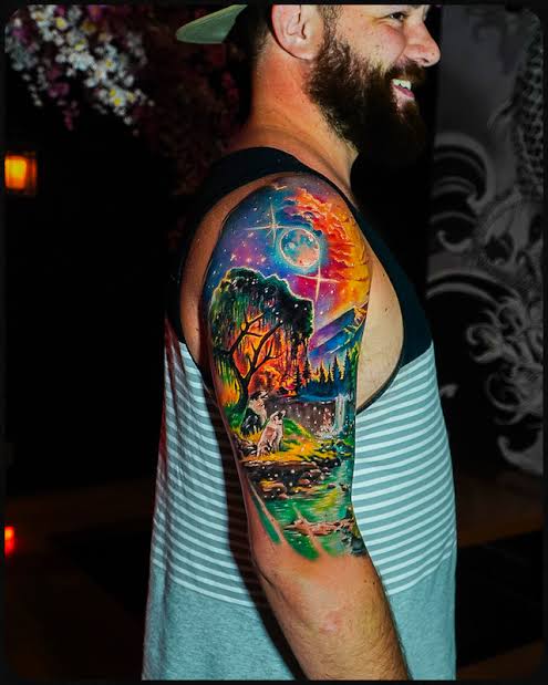 Colorful upper arm forest tattoo with a glowing moon, tree, and stream
