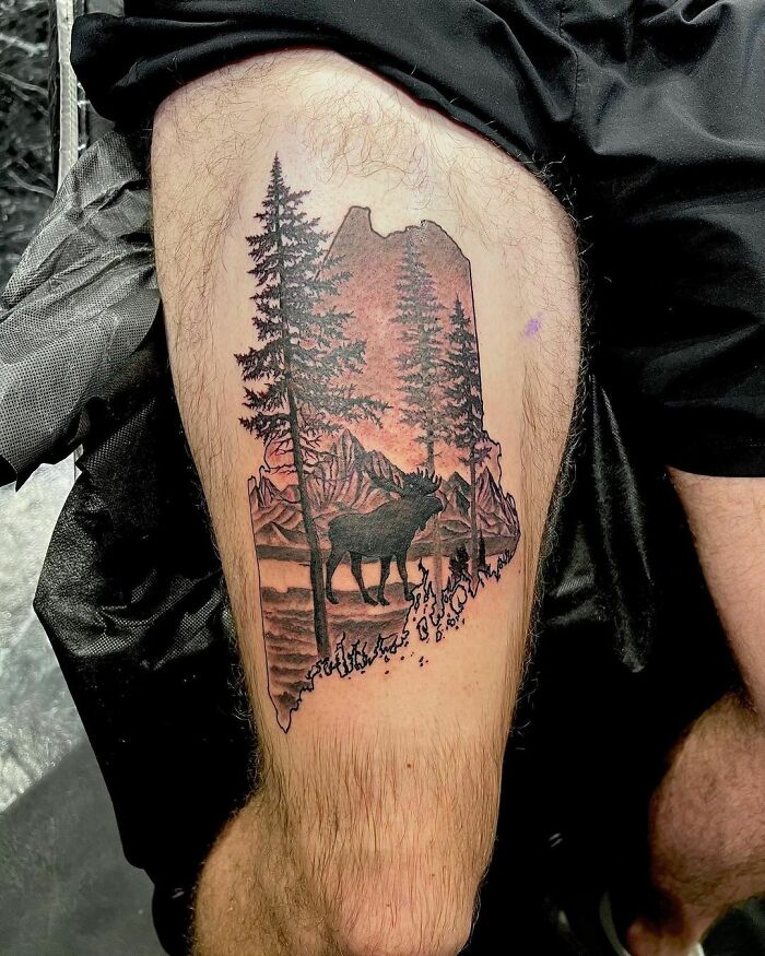 Moose among pines and mountains at sunset in a warm colored thigh tattoo