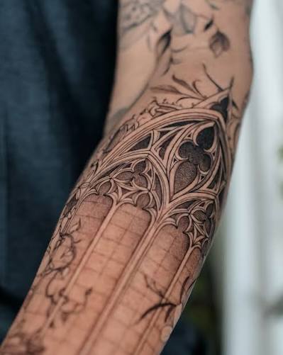 Ornate cathedral window tattoo with pointed arches and dark shading along the forearm