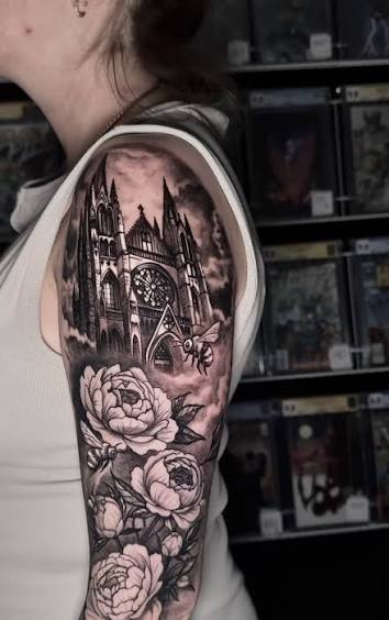 Gothic cathedral tattoo above peonies and dark leaves, wrapping the upper arm in black and gray