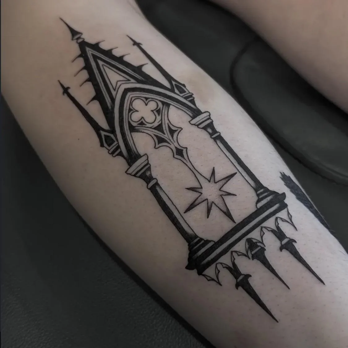 Slim cathedral window tattoo with black spires, a quatrefoil, and a starburst on the forearm