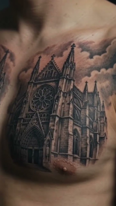 Gothic cathedral chest tattoo with sharp spires, a rose window, fine stonework, and smoky clouds