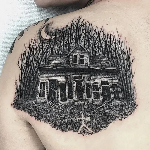 Forest swallowed haunted house tattoo on the shoulder blade shows a crumbling house surrounded by twisted bare trees.