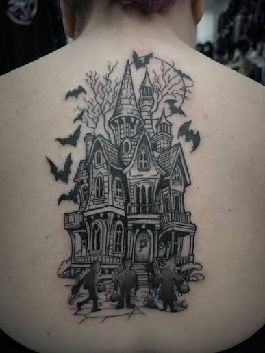 Gothic haunted manor back tattoo features towering turrets, circling bats, and three figures walking toward the porch.