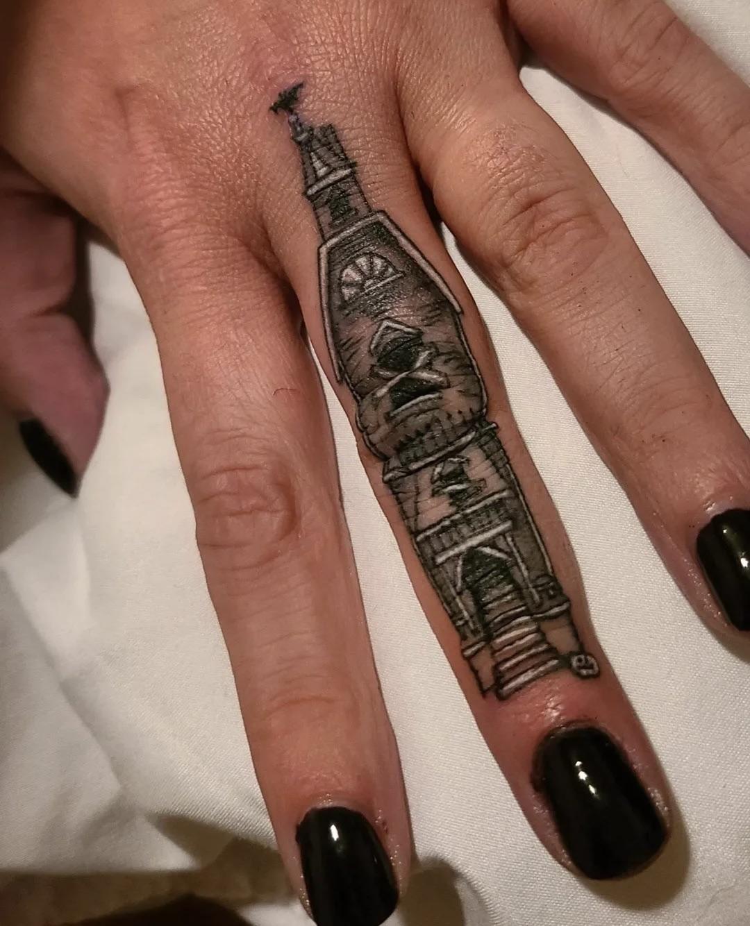Miniature haunted house finger tattoo shows a tall spooky tower in fine black and grey shading.