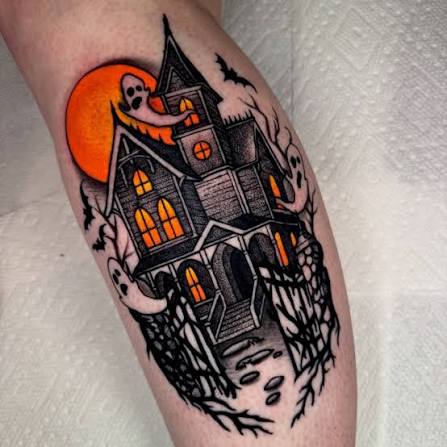 Orange moon haunted house tattoo on the calf shows lantern lit windows, peeking ghosts, and bare branches.