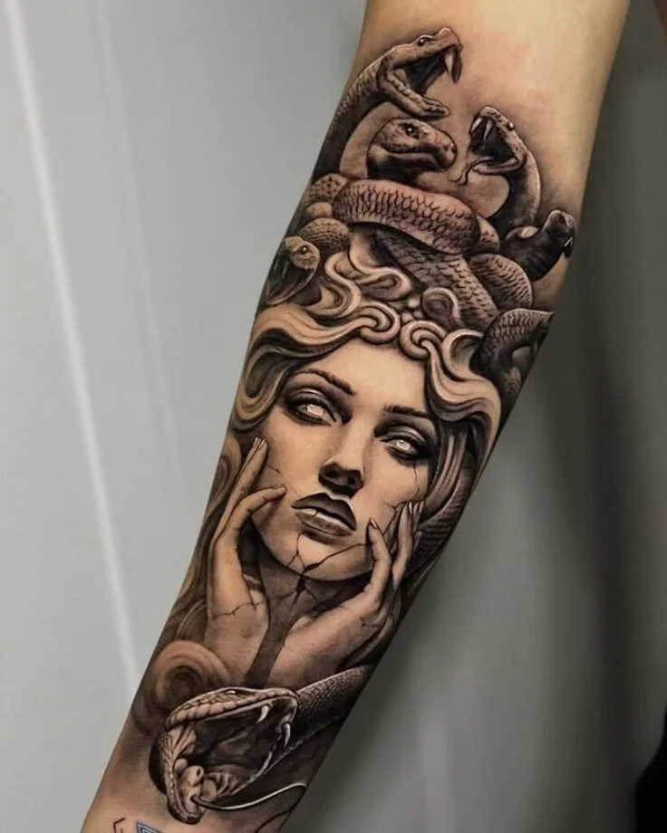 Black and gray Medusa portrait with cracked cheeks, bared fangs, and tangled snakes across the forearm.