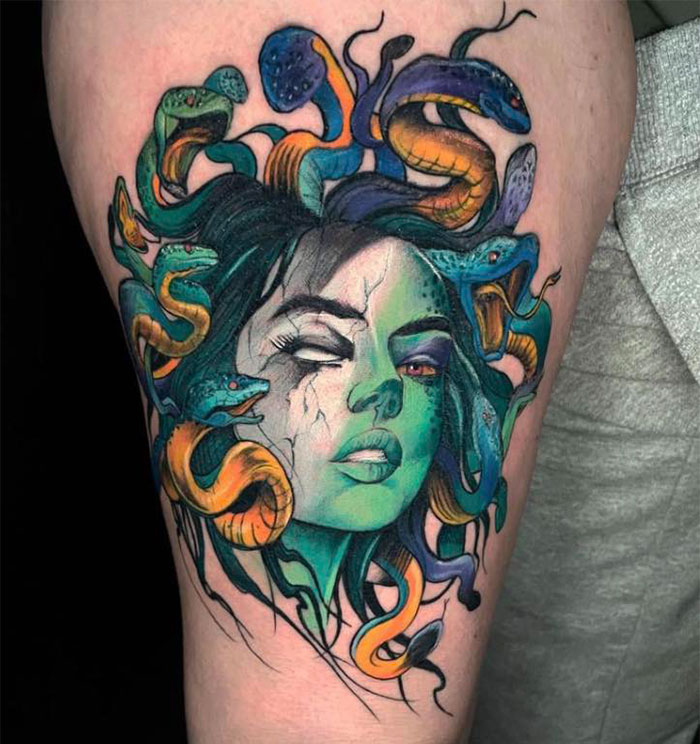 Colorful Medusa tattoo with one red eye, cracks across her face, and detailed snakes with orange bellies.