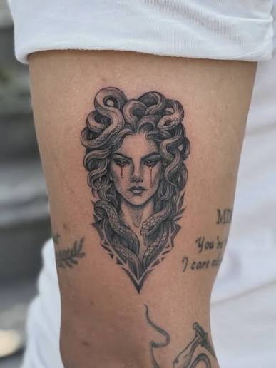 A pointed frame encloses Medusa’s stern face and looping snakes in a compact shaded arm tattoo.