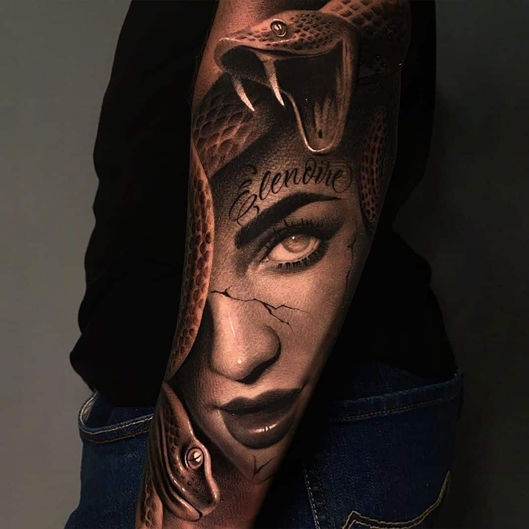 Realistic Medusa sleeve with a large snake above one visible eye, glossy lips, and script across her forehead.