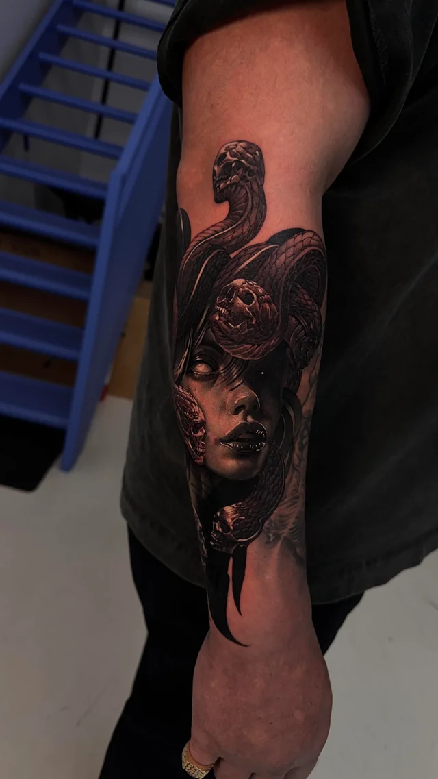 Skulls nest among dark snakes above a shaded Medusa face in an arm tattoo extending toward the wrist.