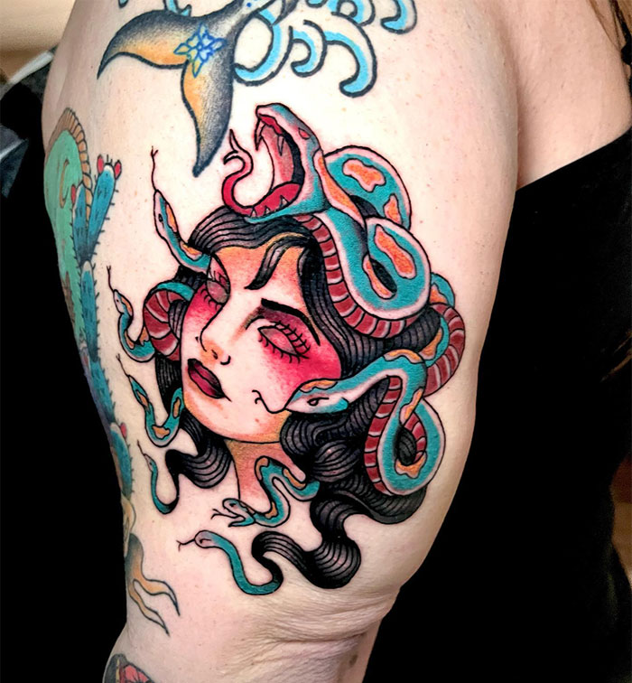 Turquoise snakes surround Medusa’s black curls and rosy cheeks, with one snake baring its fangs on the upper arm.