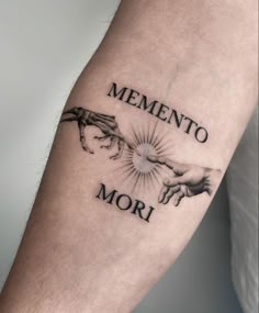Inner forearm tattoo with two reaching hands, a small sun between them, and bold memento mori lettering.