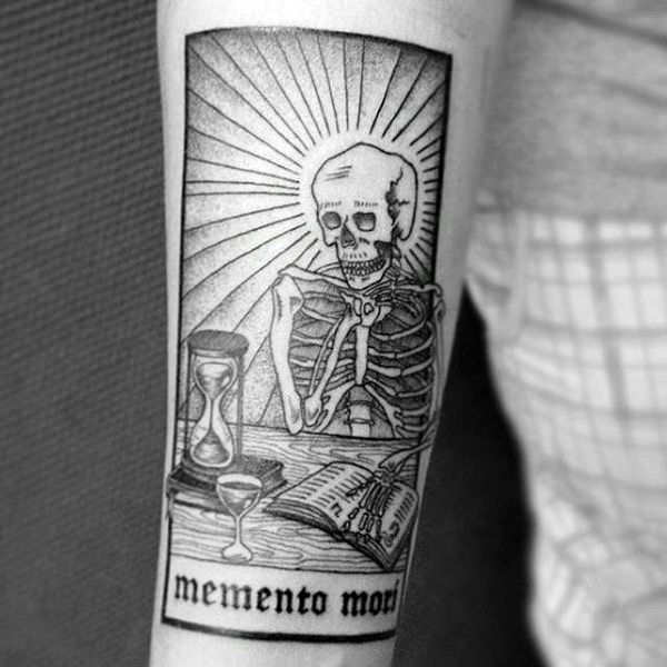 Skeleton reading a book beside an hourglass within a rectangular frame on the forearm.