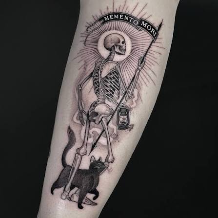 Forearm tattoo of a skeleton holding a scythe beneath a curved memento mori banner, with a black cat at its feet.