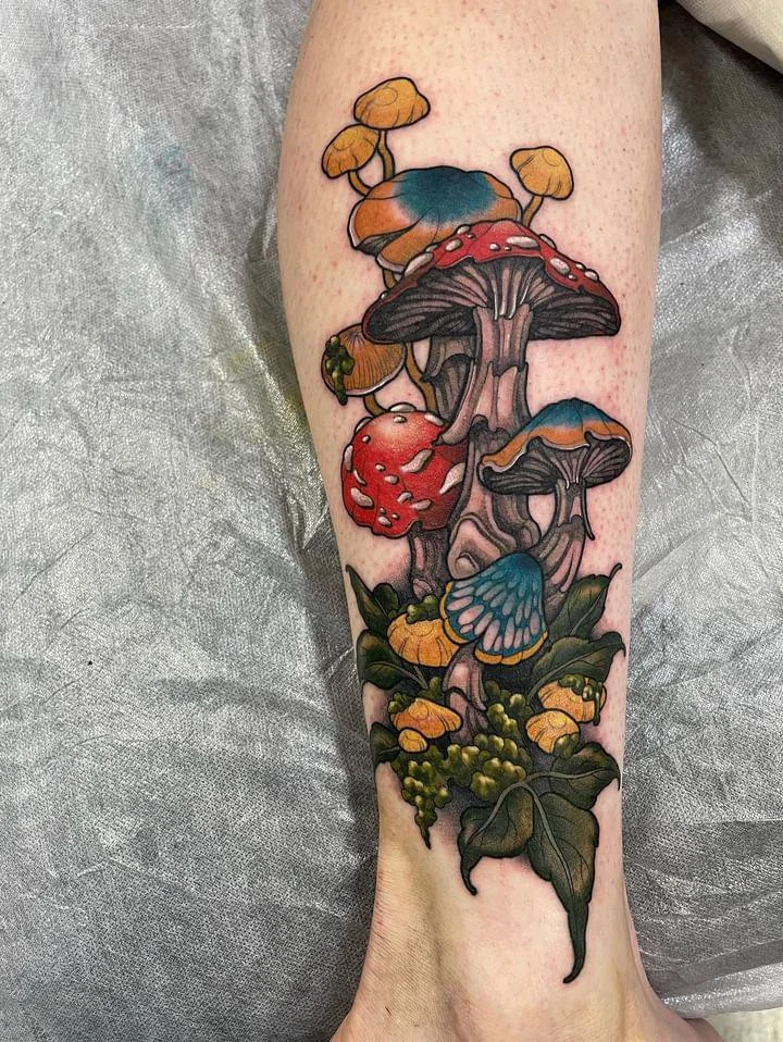 Colorful mushroom garden tattoo with red caps, blue shading, green leaves, and flowers along the lower leg.