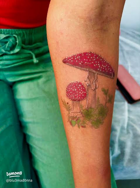 Paired red toadstools with white spots and soft greenery on the inner forearm.
