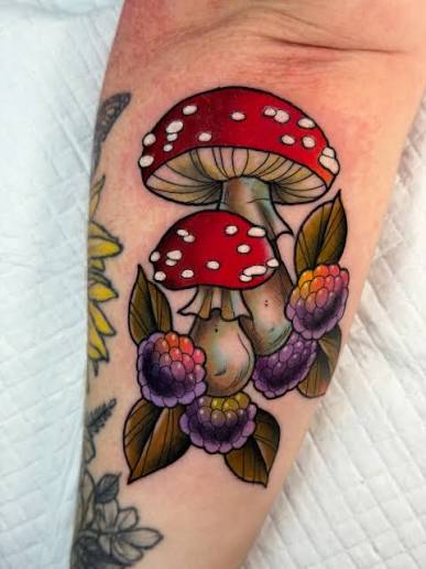 Bright red mushroom caps nestled with blackberries and bronze leaves down the inner forearm.