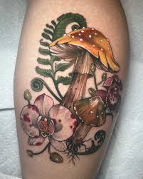 Spotted mushroom with pink flowers and curling ferns in a vertical woodland calf tattoo.