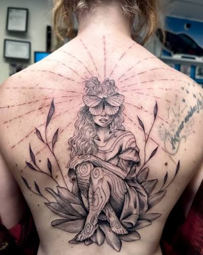 Seated woman with a moth over her eyes and broad leaves framing her back