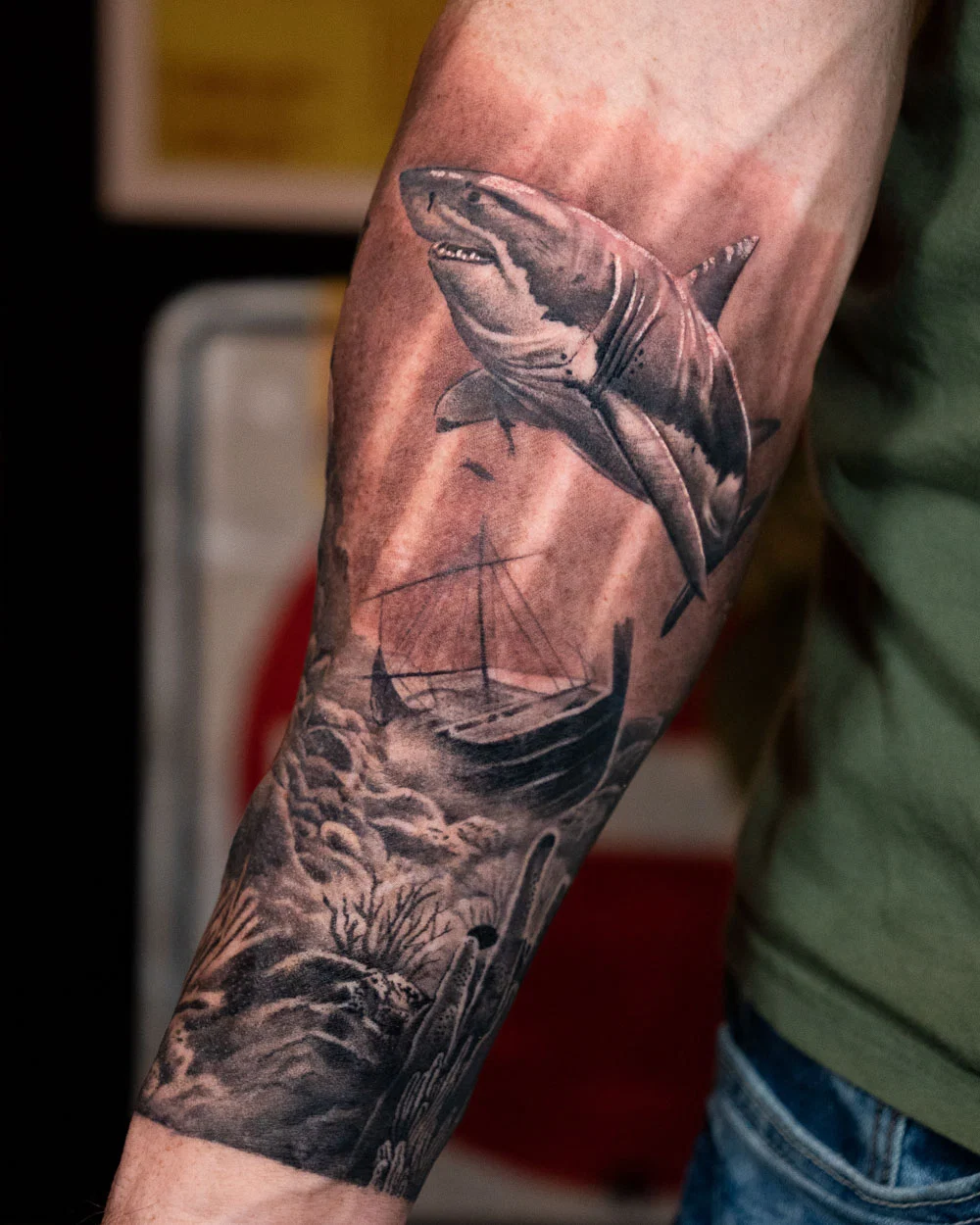 Shark looming over a sailing ship and rolling waves in a black and gray forearm tattoo