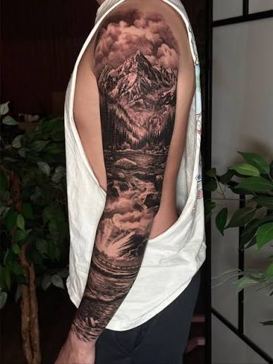 Black and gray tattoo sleeve with a rugged mountain rising through clouds above a winding stream.