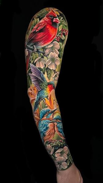 Red and blue birds sit among pink blossoms, with a cardinal high on the arm and smaller birds near the wrist.