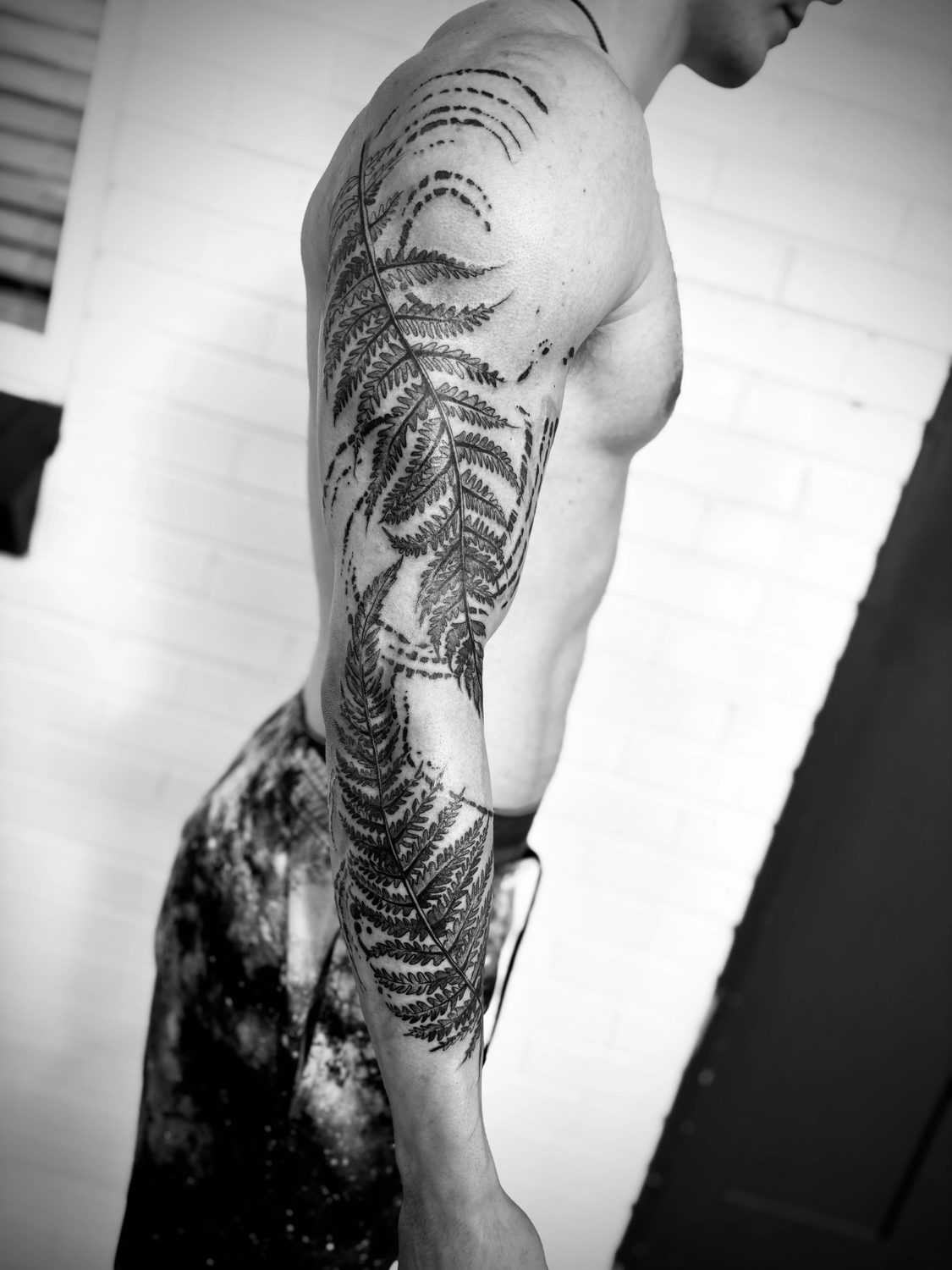 Fine fern fronds trail from shoulder to forearm, surrounded by dotted arcs.
