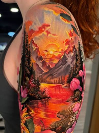 Nature tattoo sleeve with a sunset over a mountain lake, dark pines, and pink flowers on the upper arm.