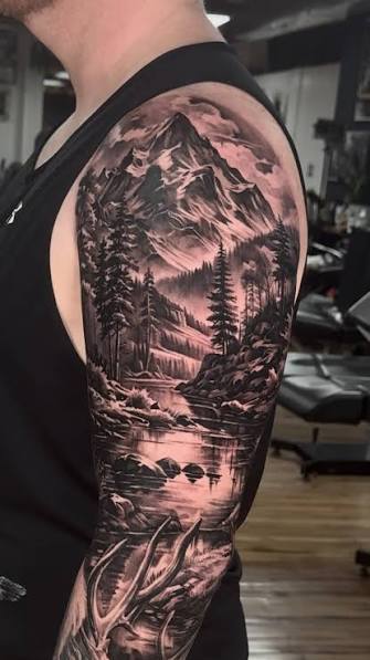 Nature tattoo sleeve with jagged mountains, pine trees, a lake, and deer antlers from shoulder to forearm.