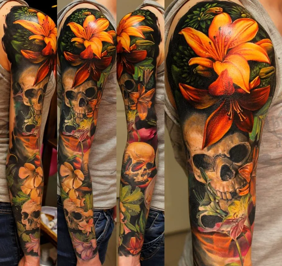 Orange lilies, dark leaves, skulls, and smaller flowers cover an arm from upper arm to wrist.