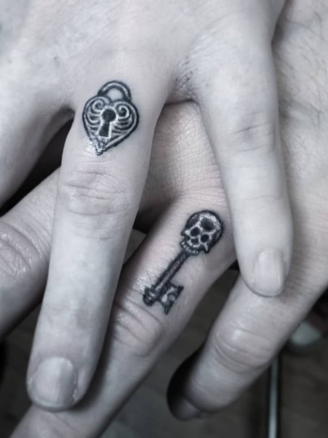 Tiny matching heart lock and skull topped key tattoos placed on the fingers