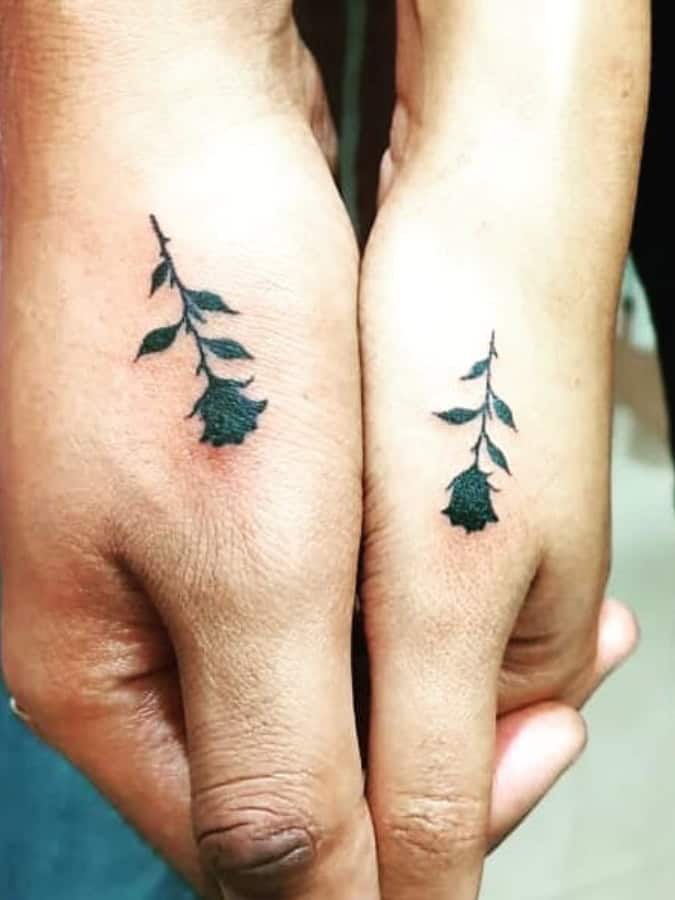 Matching drooping black rose silhouettes tattooed across the backs of joined hands