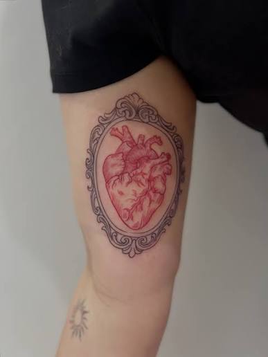 Red anatomical heart set inside an ornate vintage black frame on the upper arm