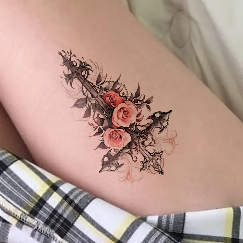 Ornate black gothic cross wrapped in blush roses and dark leaves on the upper thigh