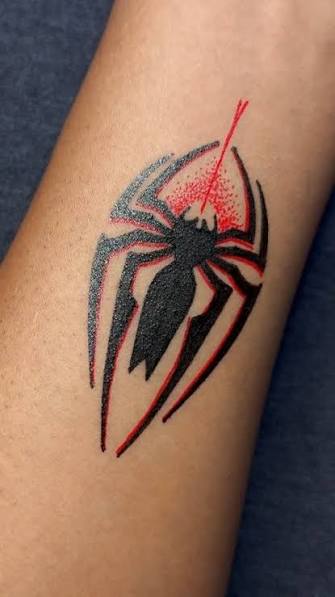 Tribal spider tattoo with jagged legs and a red gradient burst on the forearm.