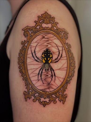 Orb weaver spider tattoo inside a cracked vintage mirror frame on the upper arm.