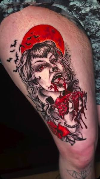 Vampire woman clutching a dripping heart beneath a red moon in a red and black thigh tattoo
